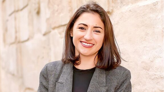 Eine junge Frau mit dunklen Haaren lächelt in die Kamera.