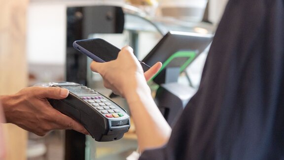 Zu sehen ist ein Kartenlesegerät, an welches eine Kundin ihre Kredit- oder EC-Karte hält, um zu bezahlen.