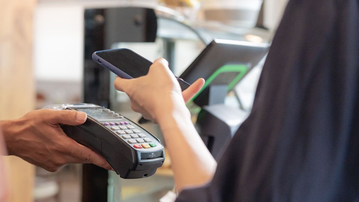 Zu sehen ist ein Kartenlesegerät, an welches eine Kundin ihre Kredit- oder EC-Karte hält, um zu bezahlen.