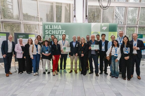 Zu sehen ist eine Gruppe Personen, die nebeneinandersteht und freundlich in die Kamera schaut. Es handelt sich um die Gewinner des Klimaschutzpartner Wettbewerbs 2026.