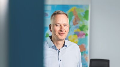 Auf dem Bild ist ein weißer Mann mit blauem Hemd und Jeanshose zu sehen.