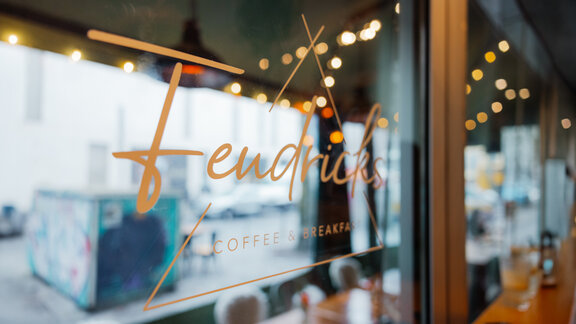 Der Fendricks-Coffee-Schriftzug am Fenster des Cafés, in dem sich der Außenbereich, Lichter und Sitzplätze spiegeln.
