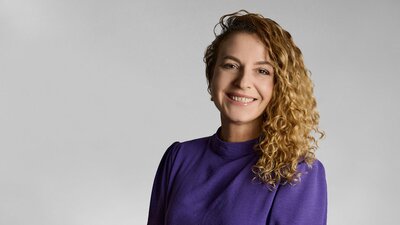 Zu sehen ist eine Frau mit lockigen Haaren und einem lila Oberteil.