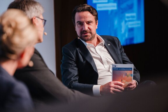 Zu sehen ist ein mittelalter Mann mit braunen Haaren und Bart in Anzug. Er sitzt und unterhält sich. Es handelt sich um den Vizepräsidenten der IHK Berlin Robert Rückel.