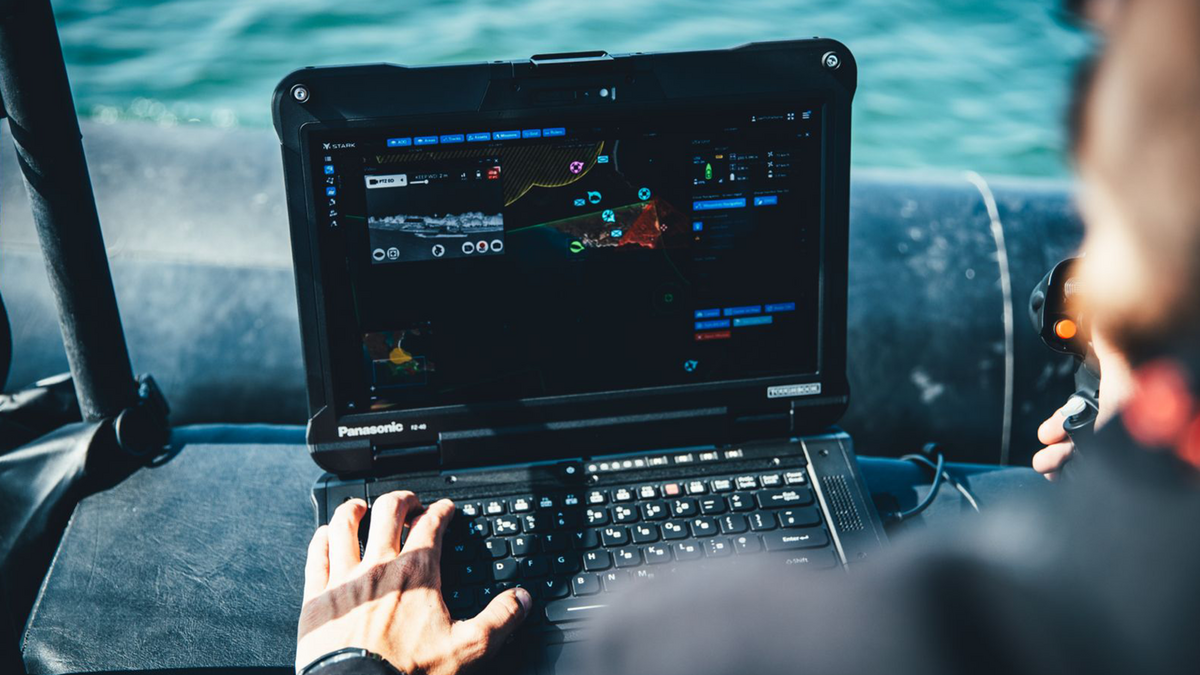 Hand einer Person bedient ein schwarzes Panasonic-Laptop mit einer komplexen, farbigen Softwareoberfläche.