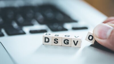 Zu sehen ist ein Teil einer Laptop-Tastatur. Darauf liegen kleine Holzwürfel mit den Buchstaben DSGVO, die dort abgelegt werden.