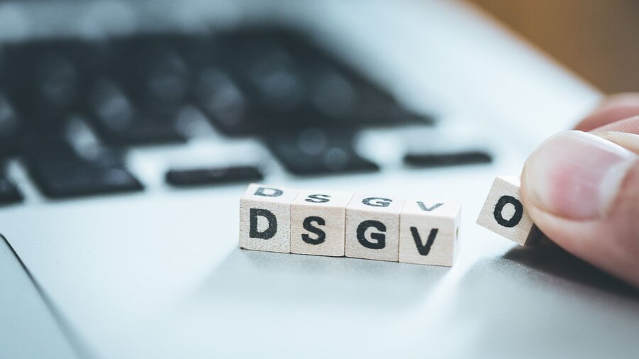 Zu sehen ist ein Teil einer Laptop-Tastatur. Darauf liegen kleine Holzwürfel mit den Buchstaben DSGVO, die dort abgelegt werden.
